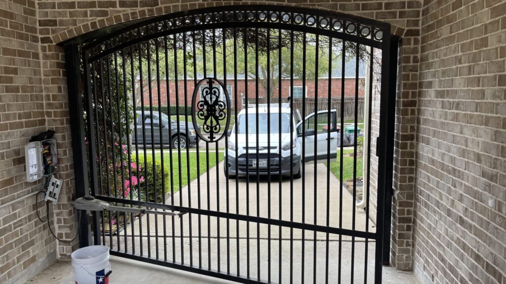 Arched iron driveway gate with a scroll centerpiece set under a brick archway
