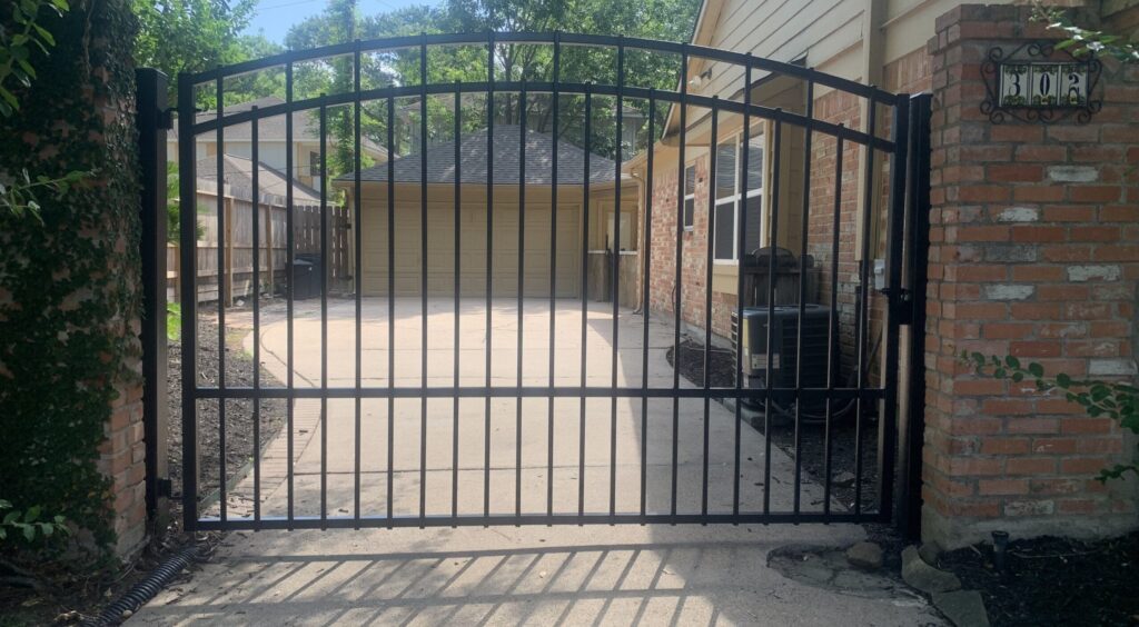 Arched iron driveway gate with keypad entry at a brick column, installed in Spring, TX