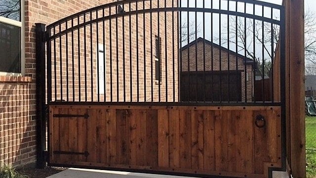 Wood and iron driveway gate with iron pickets above stained wood planks and strap hinges, installed in Atascocita, TX