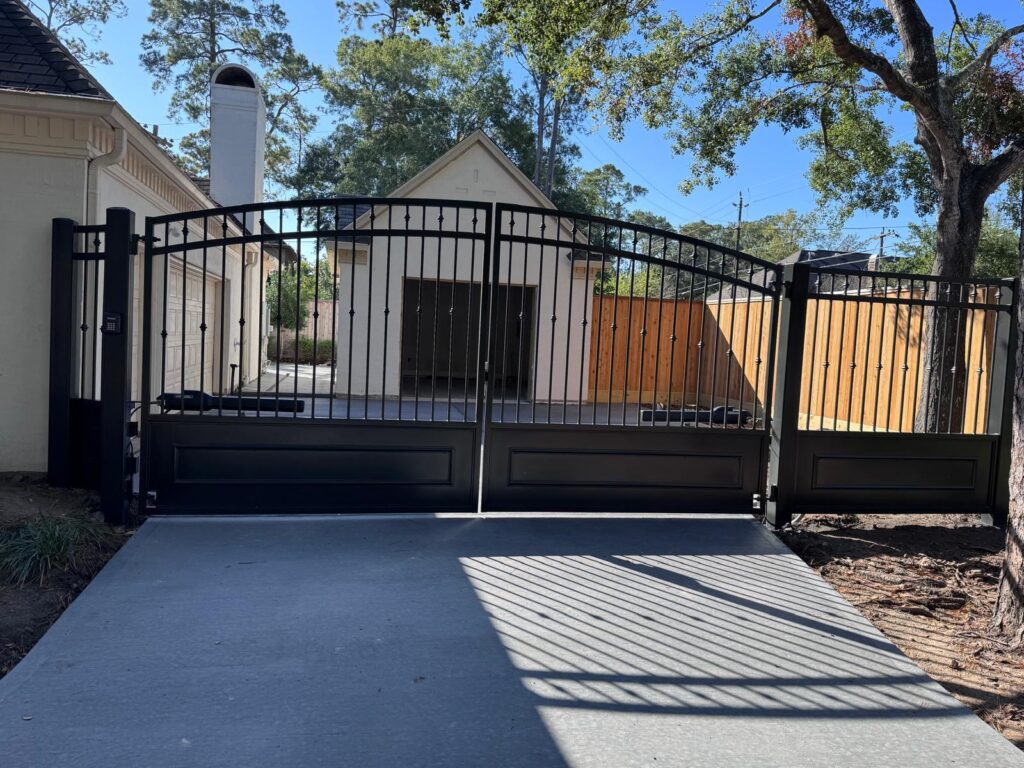 Arched wrought iron double swing gate with raised lower panels and a matching pedestrian gate, installed in Memorial, Houston, TX