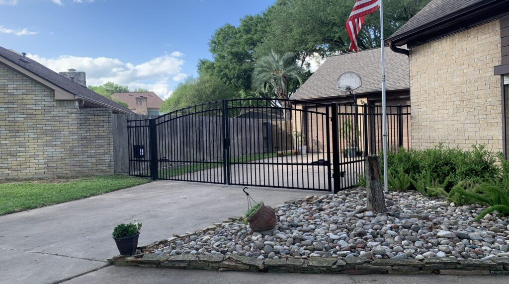 Automatic iron driveway gate at a brick home with a landscaped bed