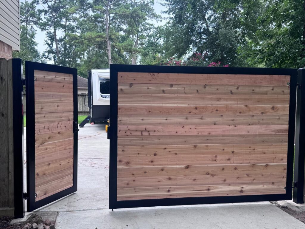 Cedar plank double driveway gate built in a welded steel frame, shown open, installed in Kingwood, TX