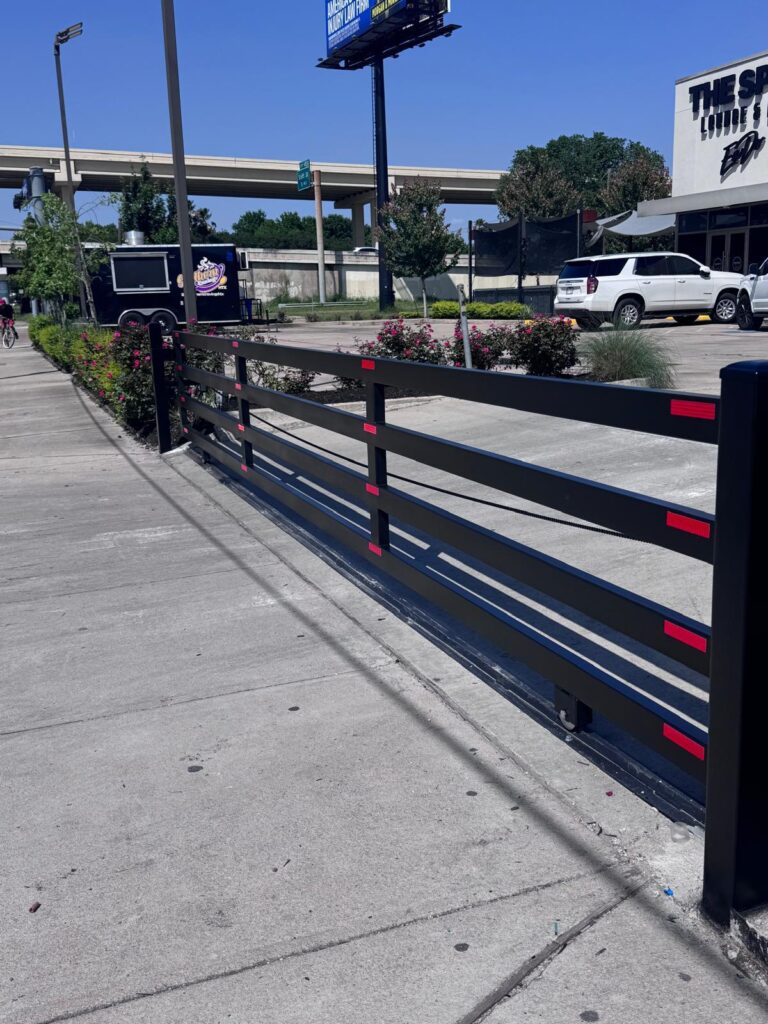 Commercial black steel slide gate on V-track with red reflectors at a retail entrance