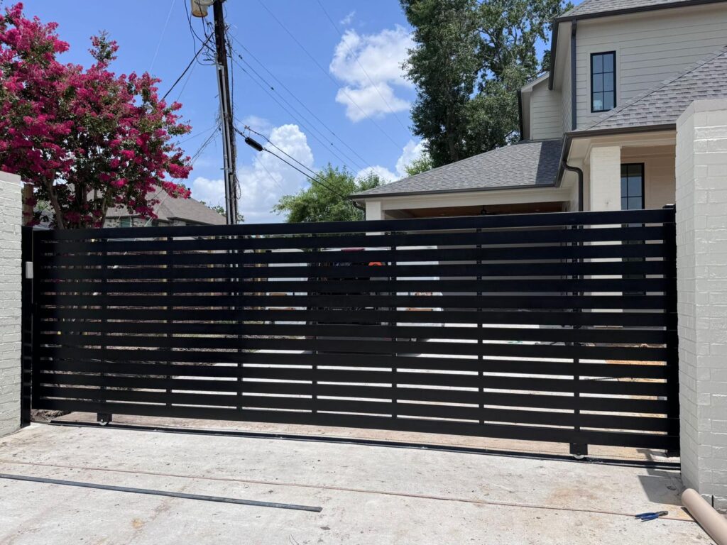 Black horizontal-slat steel slide gate on track between white painted brick columns