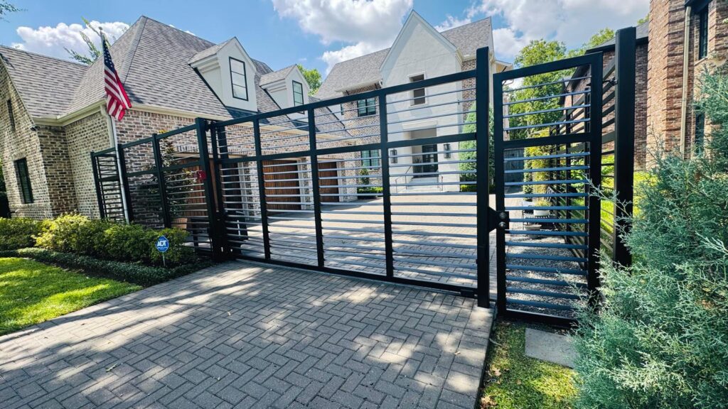 Black horizontal-slat steel swing gate and pedestrian gate on a herringbone paver driveway