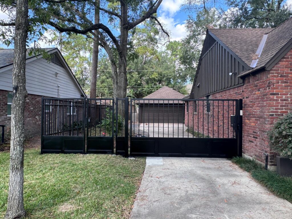 Black iron driveway gate with solid lower panels, matching fence and pedestrian gate