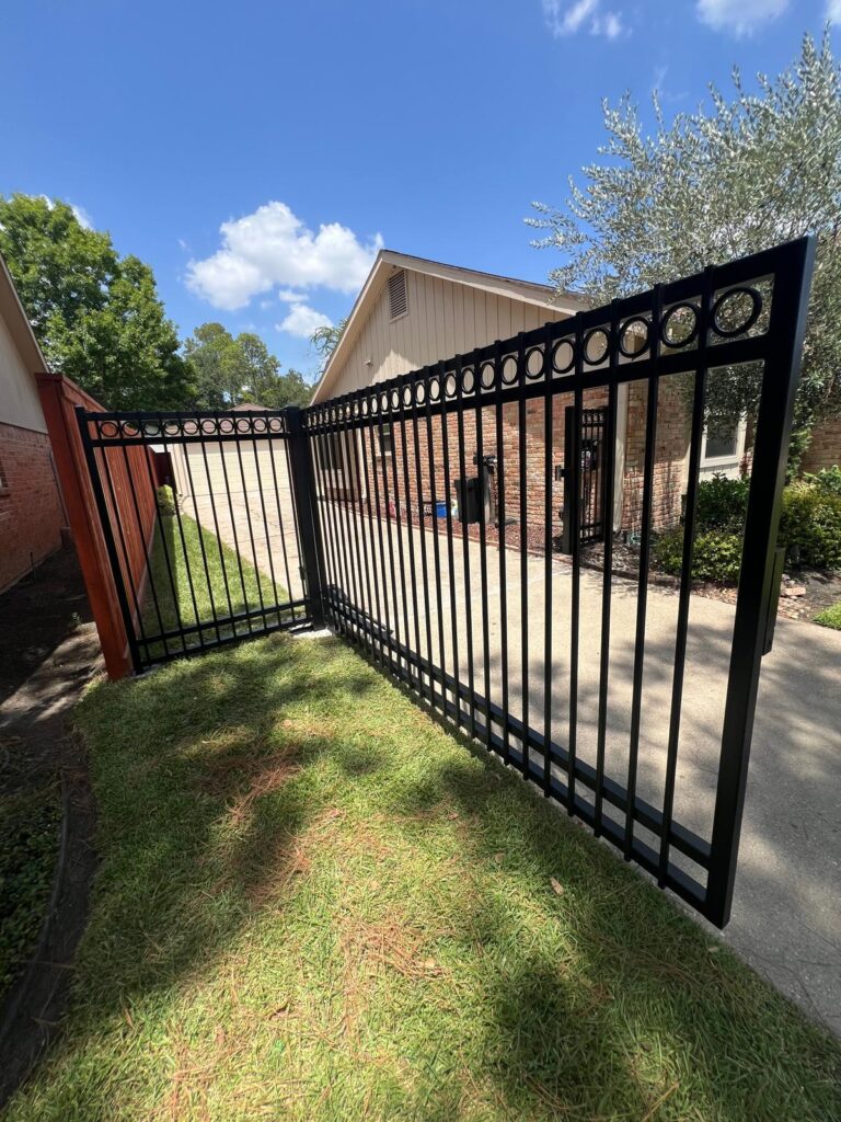 Black iron driveway gate with circle top detail, shown open, installed in Tomball, TX