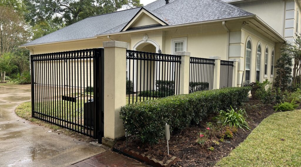 Black iron driveway gate and matching fence at a cream stucco home