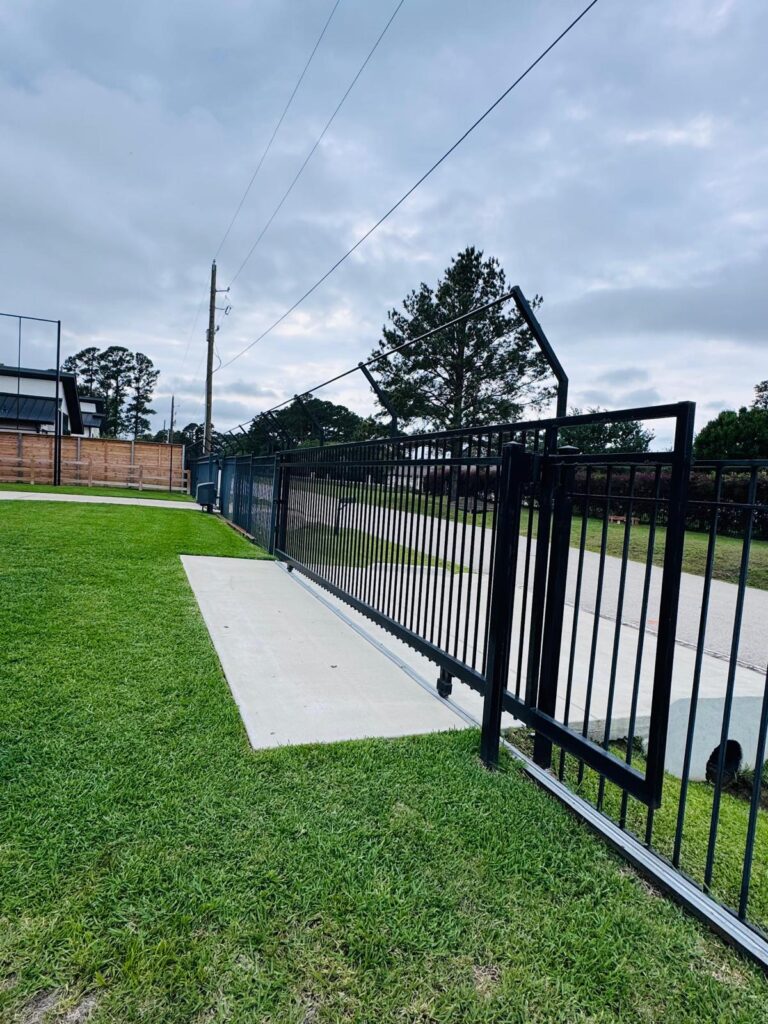 Iron slide gate running on V-track with a long matching iron fence run, installed in Conroe, TX