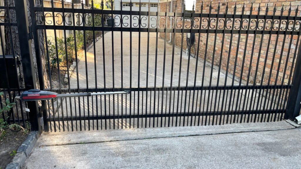 Iron double swing gate with a decorative top band and LiftMaster linear arm operator on a side driveway