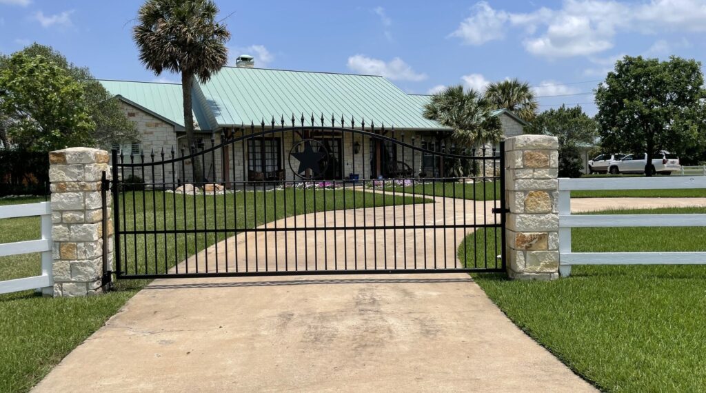 Black metal driveway gate between stone columns at a single-story ranch home