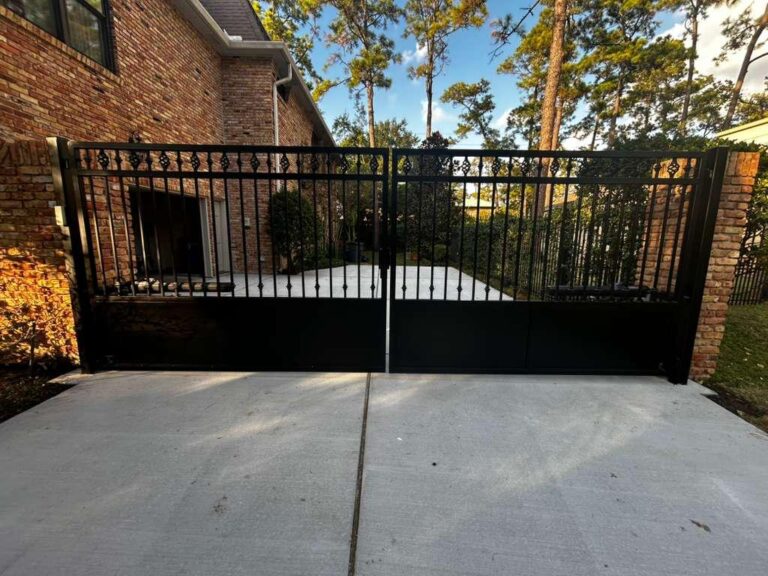 Ornamental wrought iron double driveway gate with scroll top rail and solid lower panels, installed in The Woodlands, TX