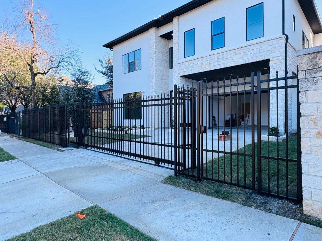 Spear-top iron slide gate and fence at a modern white stucco and limestone home